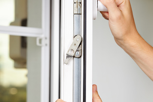 handyman adjusting white pvc plastic window indoors. worker using screwdriver to repair upvc window. homework maintenance